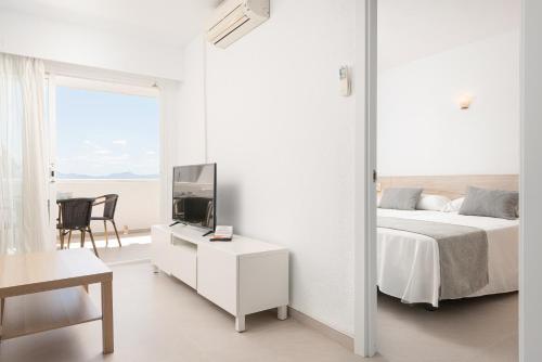 a white bedroom with a bed and a tv at Apartamentos Siesta I in Port d'Alcudia