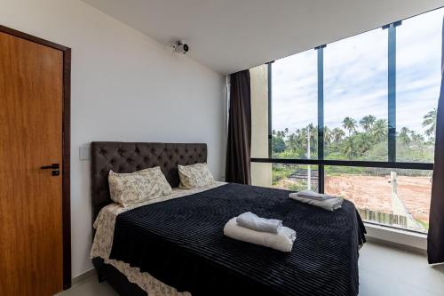 a bedroom with a black bed with a large window at Casa inteligente com 4 suítes e piscina - 160D in Japaratinga