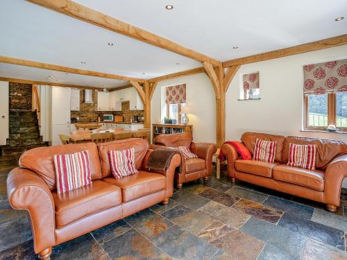 a living room with brown leather couches and a kitchen at Y Beudy - Uk49917 in Penclawdd