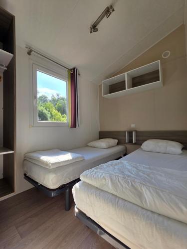 two beds in a room with a window at Camping Val de Boutonne in Saint-Jean-dʼAngély