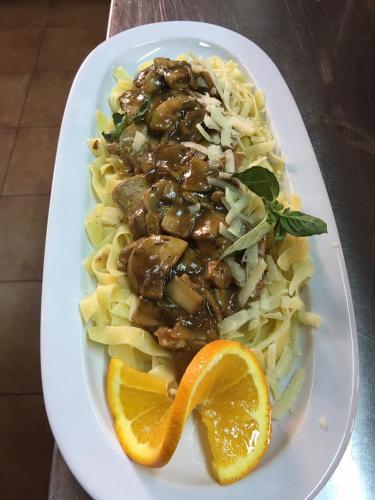 a plate of pasta with meat and an orange slice at Nymfasia Resort in Vytina