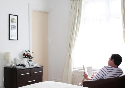 a man sitting in a chair reading a book by a window at Rockvale House in Lynton