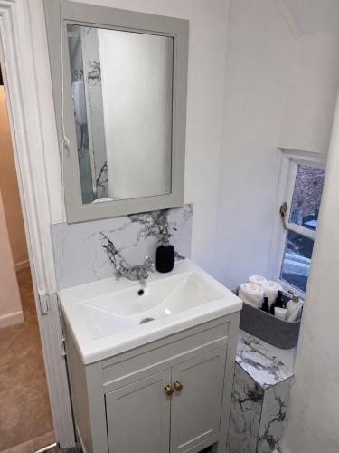 a bathroom with a white sink and a mirror at Historic High St Flat with Peaceful Garden Retreat in Stony Stratford