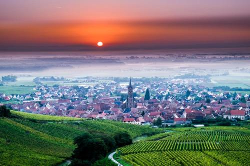 a town in the middle of a field with the sunset at Le p'tit coin de chez nous in Dambach-la-Ville