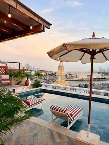 a pool with an umbrella and chairs and a clock tower at NH Royal Urban Cartagena in Cartagena de Indias