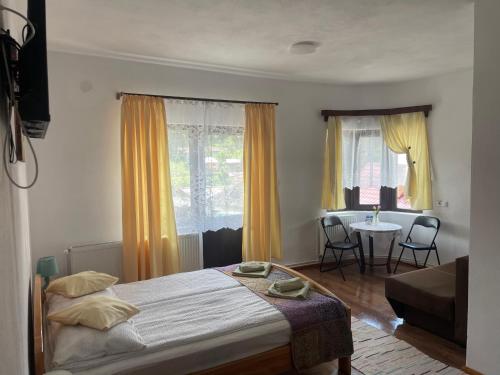 a bedroom with a bed and a table and windows at Casa Forrás in Borsec