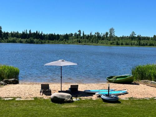 a beach with two chairs and an umbrella and a boat at Mäeküla Järve Palkmaja in Viljandi