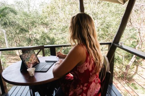 a woman sitting at a table with a laptop at Mikado Natural Lodge in Playa Avellana