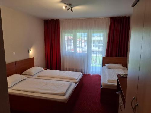 two beds in a hotel room with red curtains at Pensiune Safrane in Băile Herculane