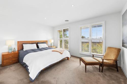 a bedroom with a bed and a chair and windows at Willos in Queenscliff