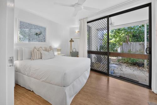a white bedroom with a large bed and a sliding glass door at Suntan at Sunshine in Sunshine Beach