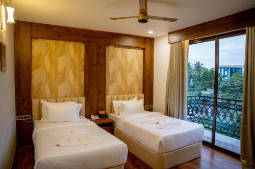 a bedroom with two beds and a window with a balcony at Raphilhin The Business Hotel in Perintalmanna