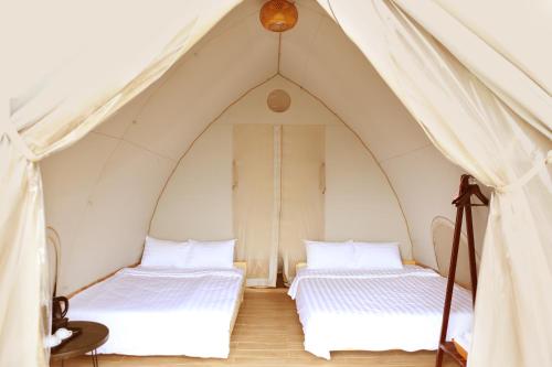 two beds in a tent with white sheets at NSH Riverside Glamping Resort in Hanoi