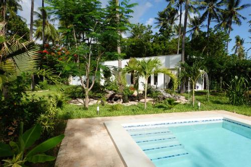 a swimming pool in front of a house with trees at Nyotas gem in Watamu