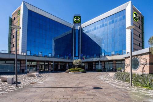 a large glass building with a clock in front of it at B&B HOTEL Expo Verona Villafranca in Villafranca di Verona