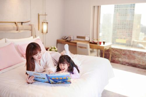 a woman and a little girl laying on a bed reading a book at China World Hotel, Beijing, A Shangri-La Hotel in Beijing