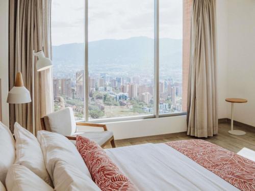 a hotel room with a bed and a large window at Novotel Medellin El Tesoro in Medellín