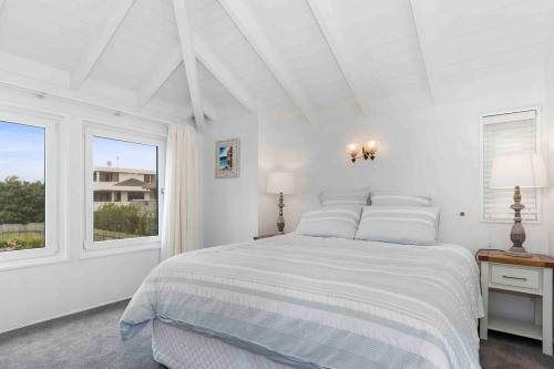 a white bedroom with a bed and two windows at Beachfront Marine Parade in Mount Maunganui