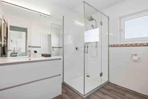 a white bathroom with a shower and a sink at Beachfront Marine Parade in Mount Maunganui