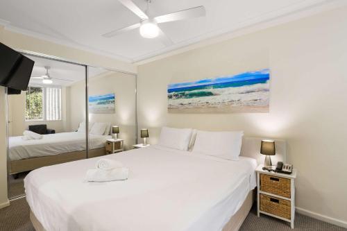 a white bedroom with two beds and a tv at Solara at Aqua Mantra in Nelson Bay