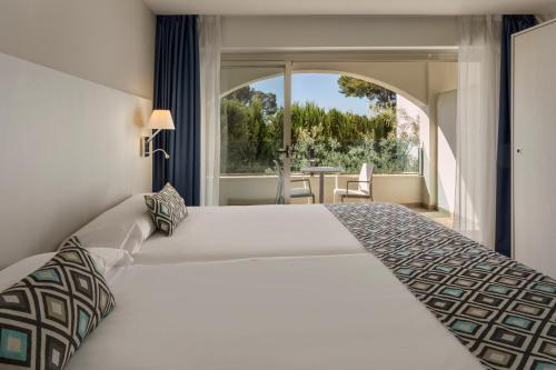 una camera da letto con un grande letto bianco e una grande finestra di Alcanada Golf Hotel a Port d'Alcudia