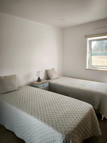 two beds in a white room with a window at A Quinta in Vila Nova de Milfontes