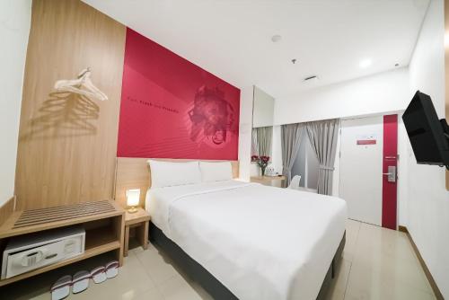 a bedroom with a white bed and a red wall at favehotel Pluit Junction in Jakarta