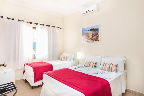 two beds in a white room with red sheets at Hotel Pousada Vivendas do Sol e Mar in Caraguatatuba