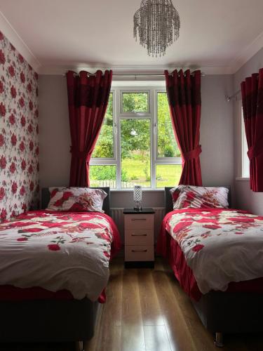 two beds in a bedroom with red curtains and a window at Glenmount Castleblayney in Castleblayney