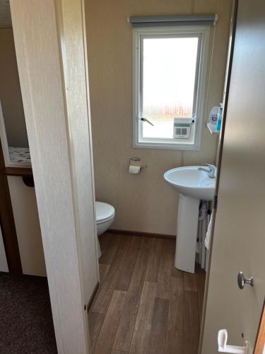 a bathroom with a toilet and a sink and a window at California cliffs caravan in Great Yarmouth