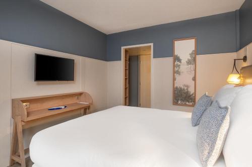 a bedroom with a white bed and a television at Hôtel Arcanse by Inwood Hotels in Arcachon