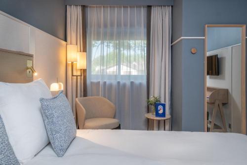 a hotel room with a bed and a chair and a window at Hôtel Arcanse by Inwood Hotels in Arcachon