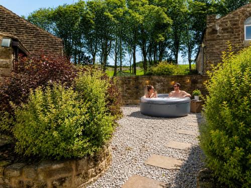two people in a bath tub in a garden at The Bronte Moor Retreat - 3 Bed, Pet Friendly Cottage - Stunning Views - Hot Tub in Heptonstall