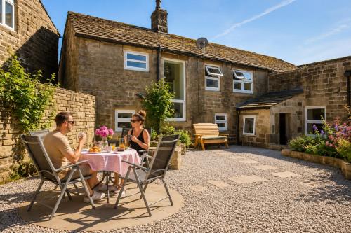 two people sitting at a table in front of a house at The Bronte Moor Retreat - 3 Bed, Pet Friendly Cottage - Stunning Views - Hot Tub in Heptonstall
