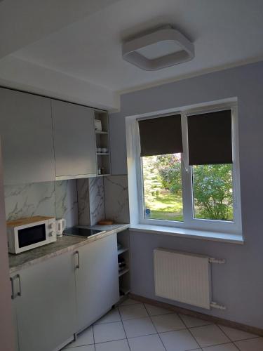 a kitchen with white cabinets and a microwave and a window at Apartament orhideja 11 in Riga