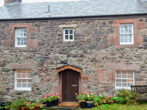 an old stone house with flowers in front of it at Willesdene Cottage in Abernethy
