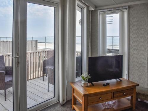 a living room with a television and a balcony at Sandbank in Bacton
