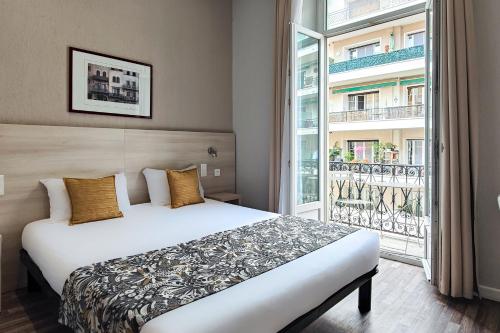 a bedroom with a bed and a large window at Hôtel Helvétique in Nice