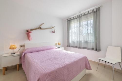 a white bedroom with a pink bed and a white chair at Planta baja Marita in Deltebre