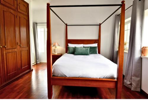 a bedroom with a canopy bed with white sheets and green pillows at Casa do Sol Wellness Home in Óbidos