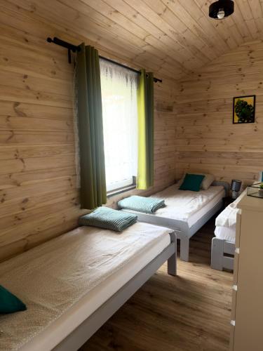 two beds in a wooden room with a window at Domki u Czopera in Zełwągi