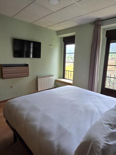 a bedroom with a large white bed and two windows at Hostal La Cigüeña in El Espinar