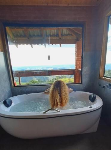 a person in a bath tub with a window at Chalé Theo - Para momentos únicos in Camanducaia
