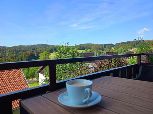 a cup of coffee sitting on a wooden table on a balcony at SONNENSEITE Schonach - Private Infrarot-Sauna - Schwarzwald-Panoramablick - 2 separate Schlafzimmer - Ruhige Lage am Waldrand in Schonach