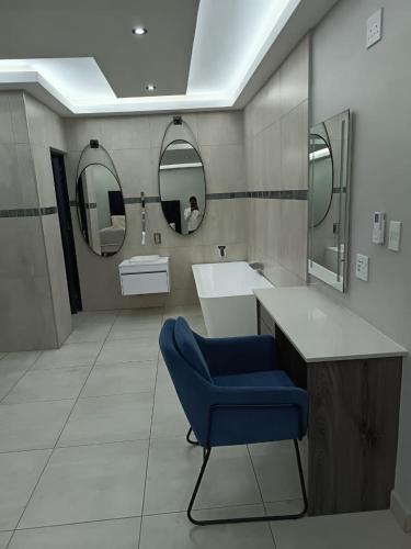 a bathroom with a blue chair and a sink and mirrors at New Hillcrest centre guest House in Kimberley