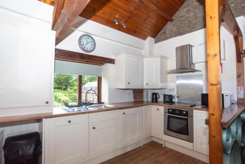 a kitchen with white cabinets and a clock on the wall at Treetop View - Old Mill Cottages in Ilfracombe