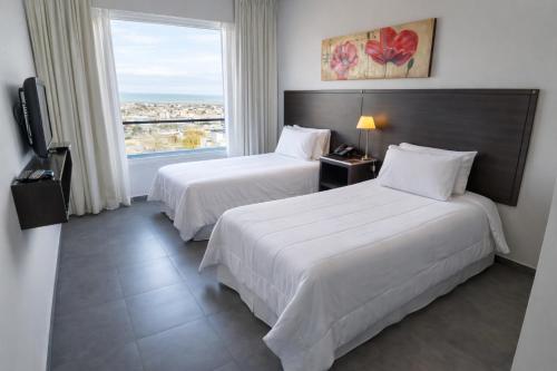 two beds in a hotel room with a window at Hotel NEU 354 in Neuquén