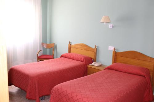 two beds in a hotel room with red sheets at Hostal Sandino in Villodrigo