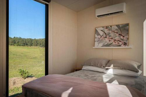 a bedroom with a bed and a large window at Tiny Tallowood by Tiny Away in Glenreagh