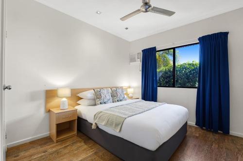 a bedroom with a bed with blue curtains and a window at Dunes Escape in Broome